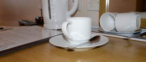 A table with a white coffee maker, a white mug, and two white cups on saucers, along with a spoon and a menu.