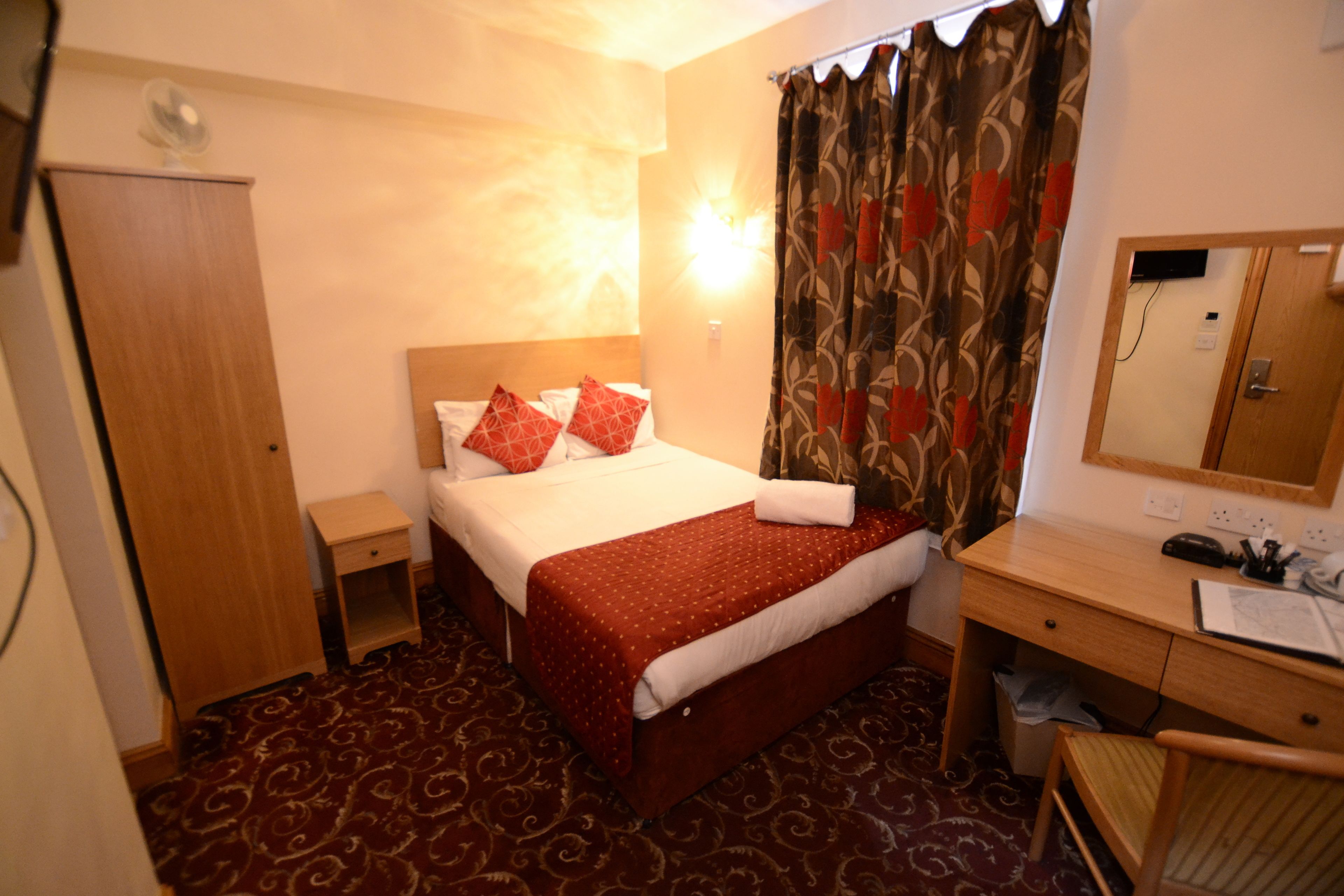 Una habitación de hotel con cama, mesita de noche, escritorio, silla y espejo.