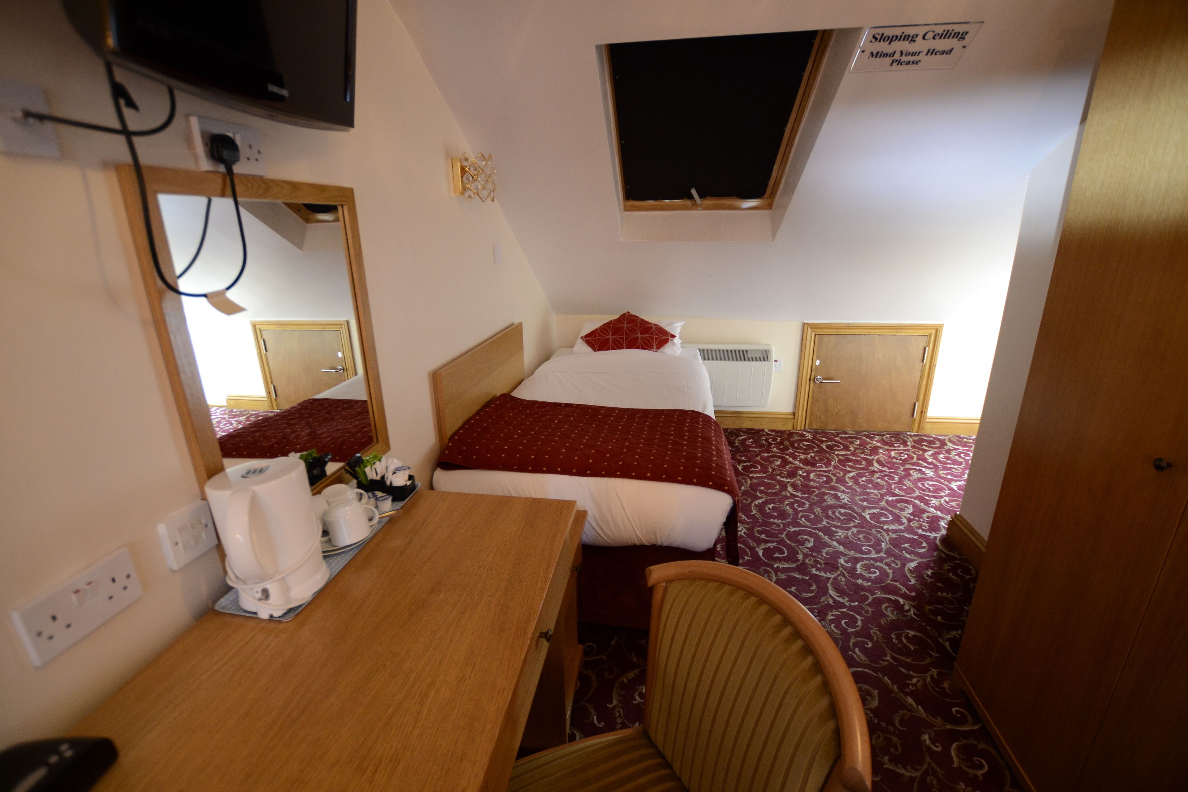 Une chambre d’hôtel avec un lit, un bureau et une chaise, un téléviseur fixé au mur et une fenêtre sur laquelle est apposée une pancarte.