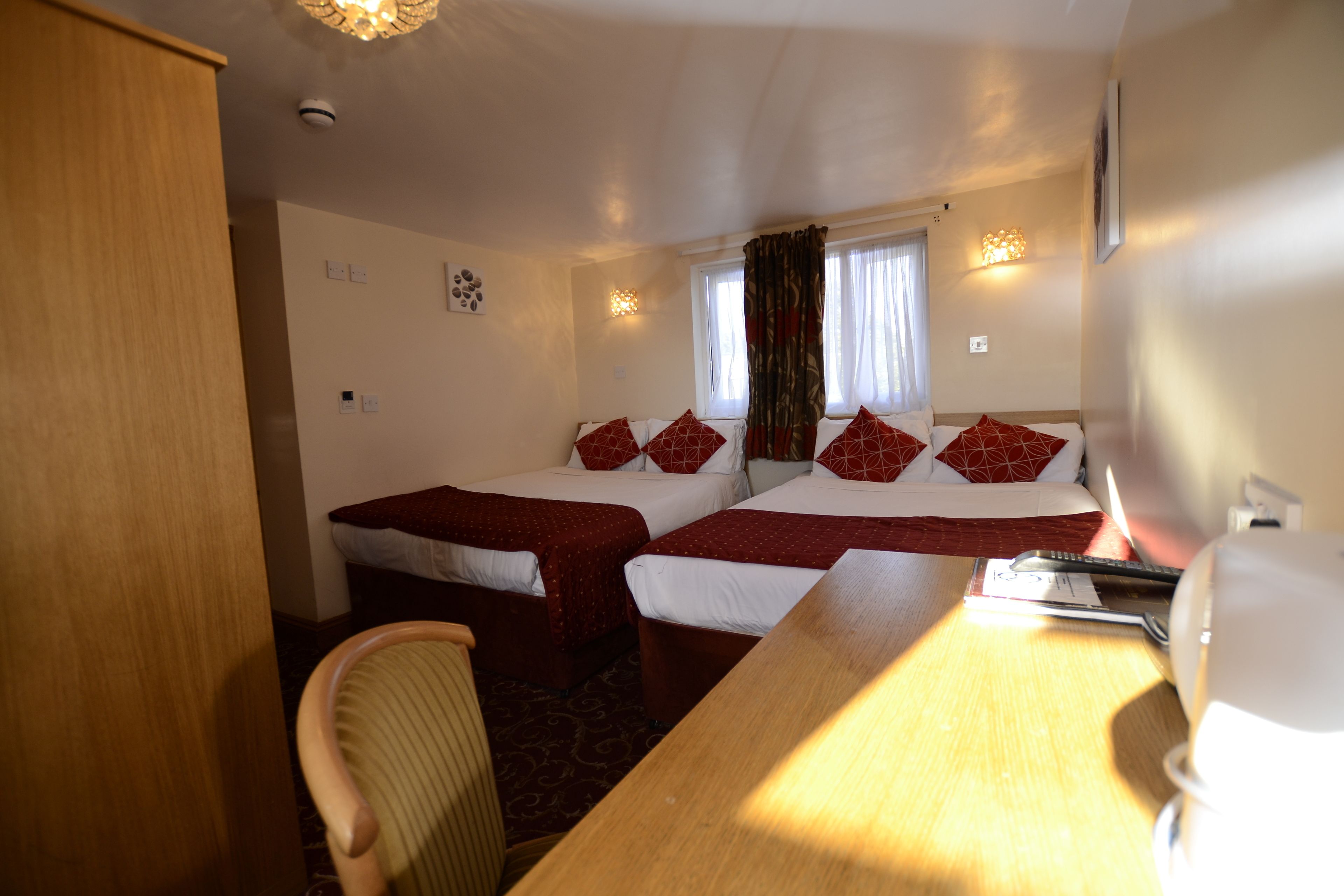 A hotel room with two beds, a wooden desk, a chair, and a window with curtains.