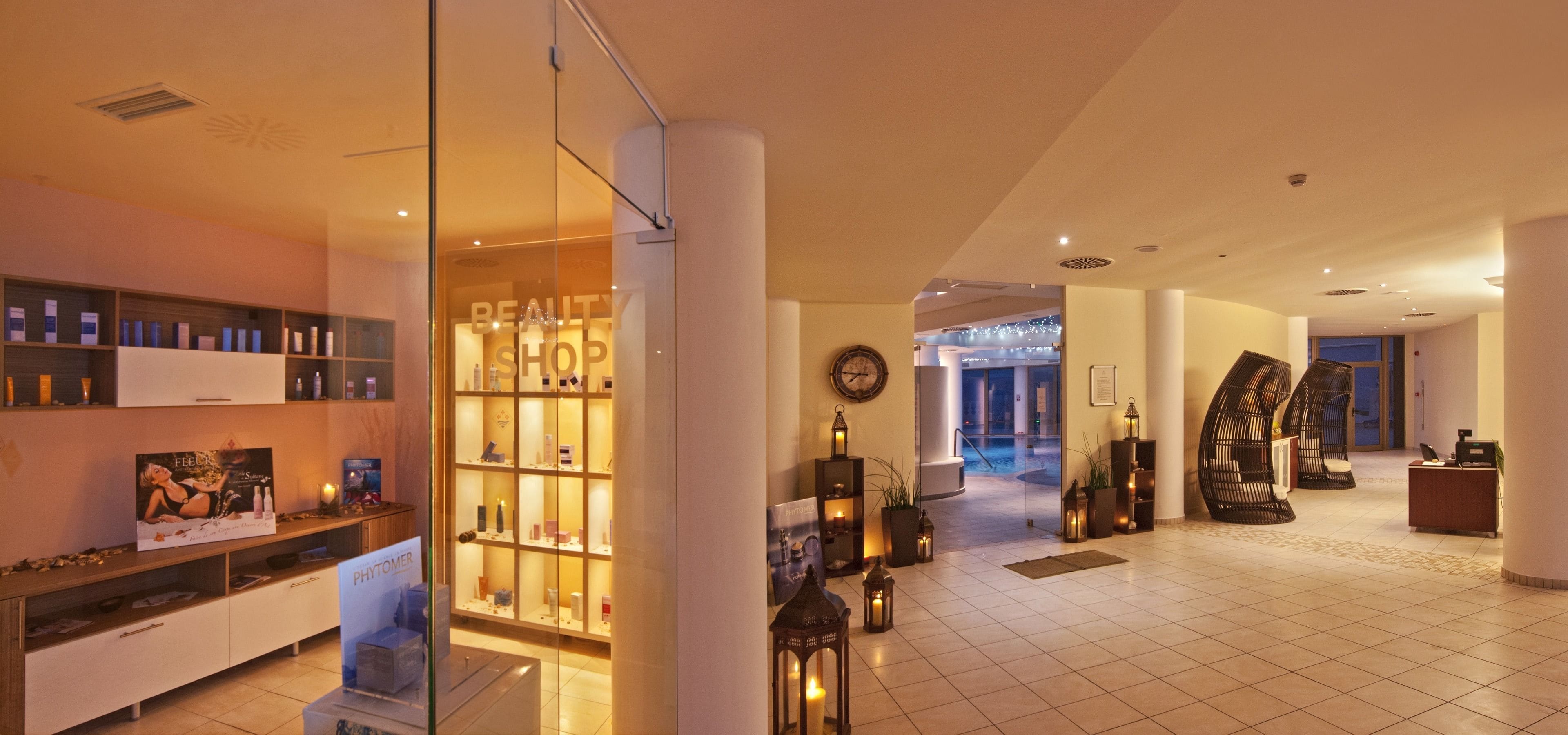 Eine Hotelhalle mit einem Schönheitssalon, einem Empfangsbereich und einem durch eine Glaswand einsehbaren Poolbereich.