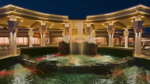 Ein Hotel bei Nacht mit einem zentralen Wasserspiel, mehreren Balkonstufen und einer gut beleuchteten Fassade.
