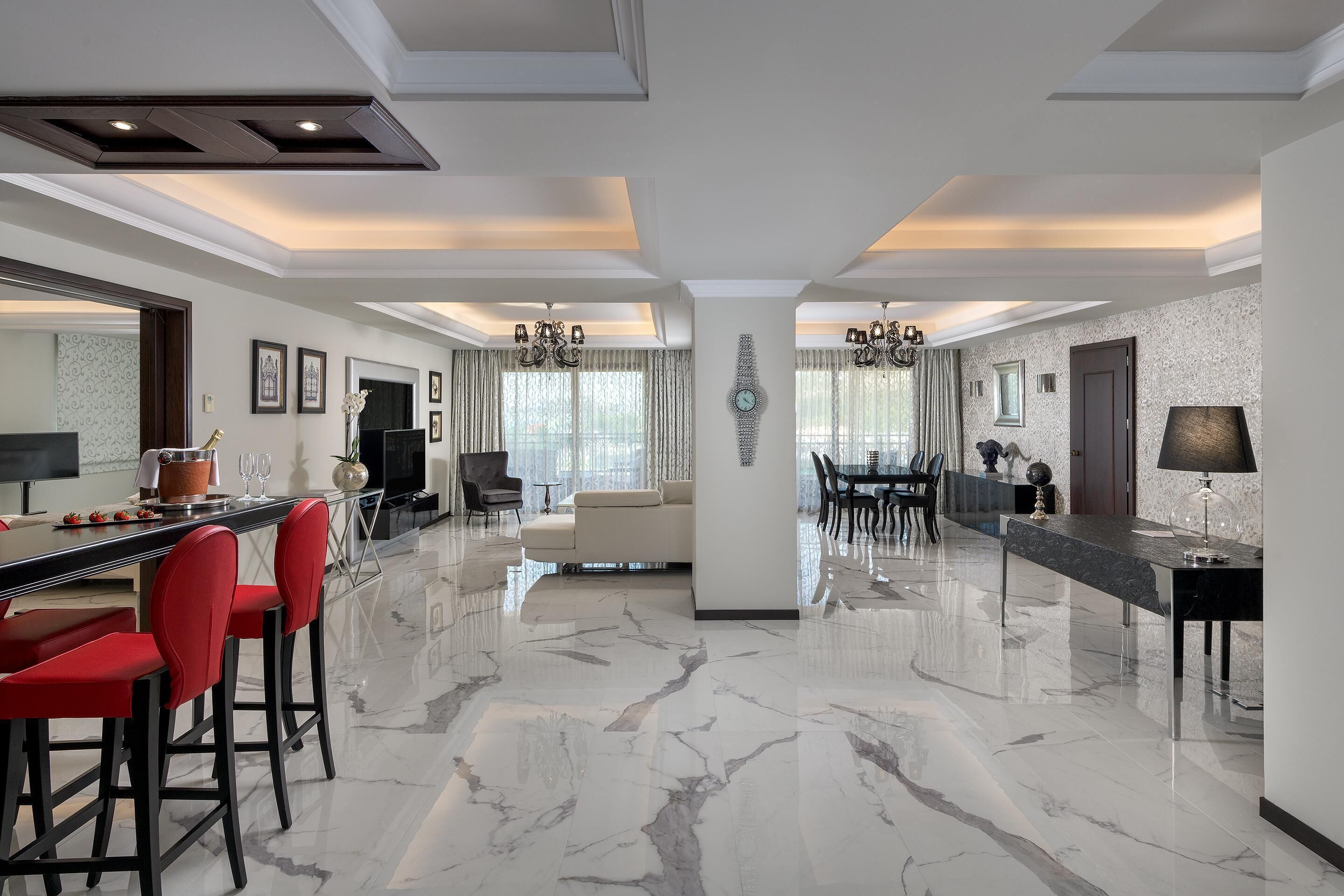 Amplia sala de estar con piso de mármol, una mesa de comedor, taburetes rojos, un sofá y un espejo grande.