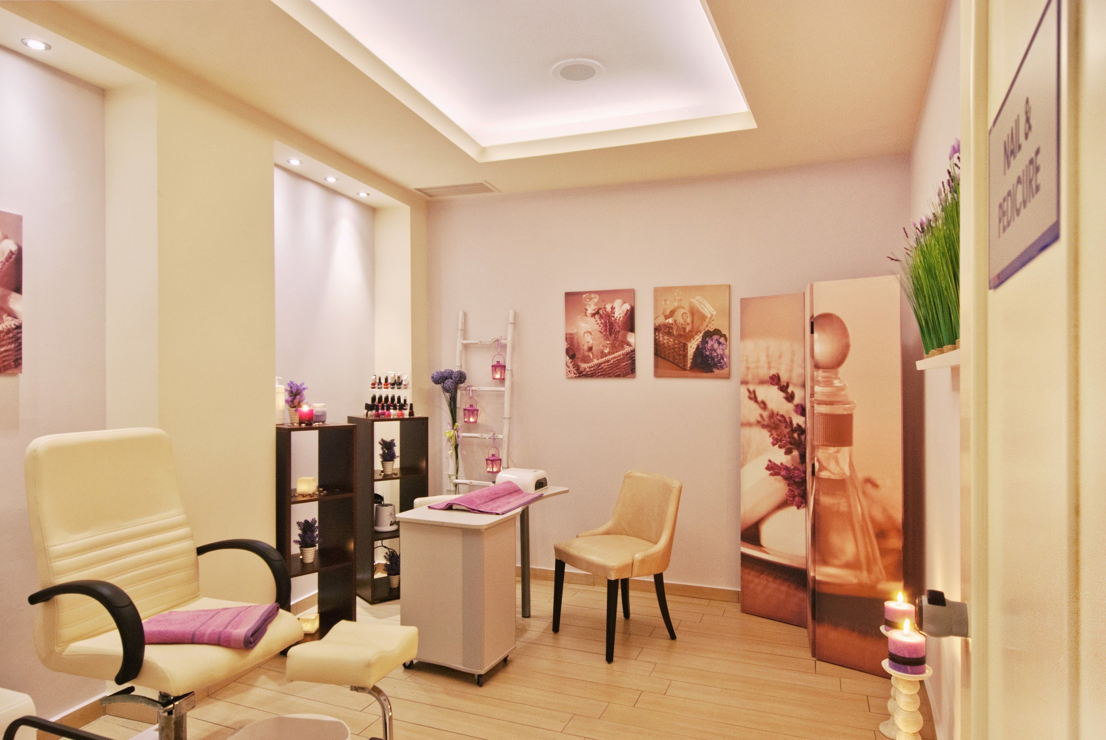 Een goed verlichte salon met een receptiebalie, twee stoelen, een plank met schoonheidsproducten en ingelijste kunstwerken aan de muren.