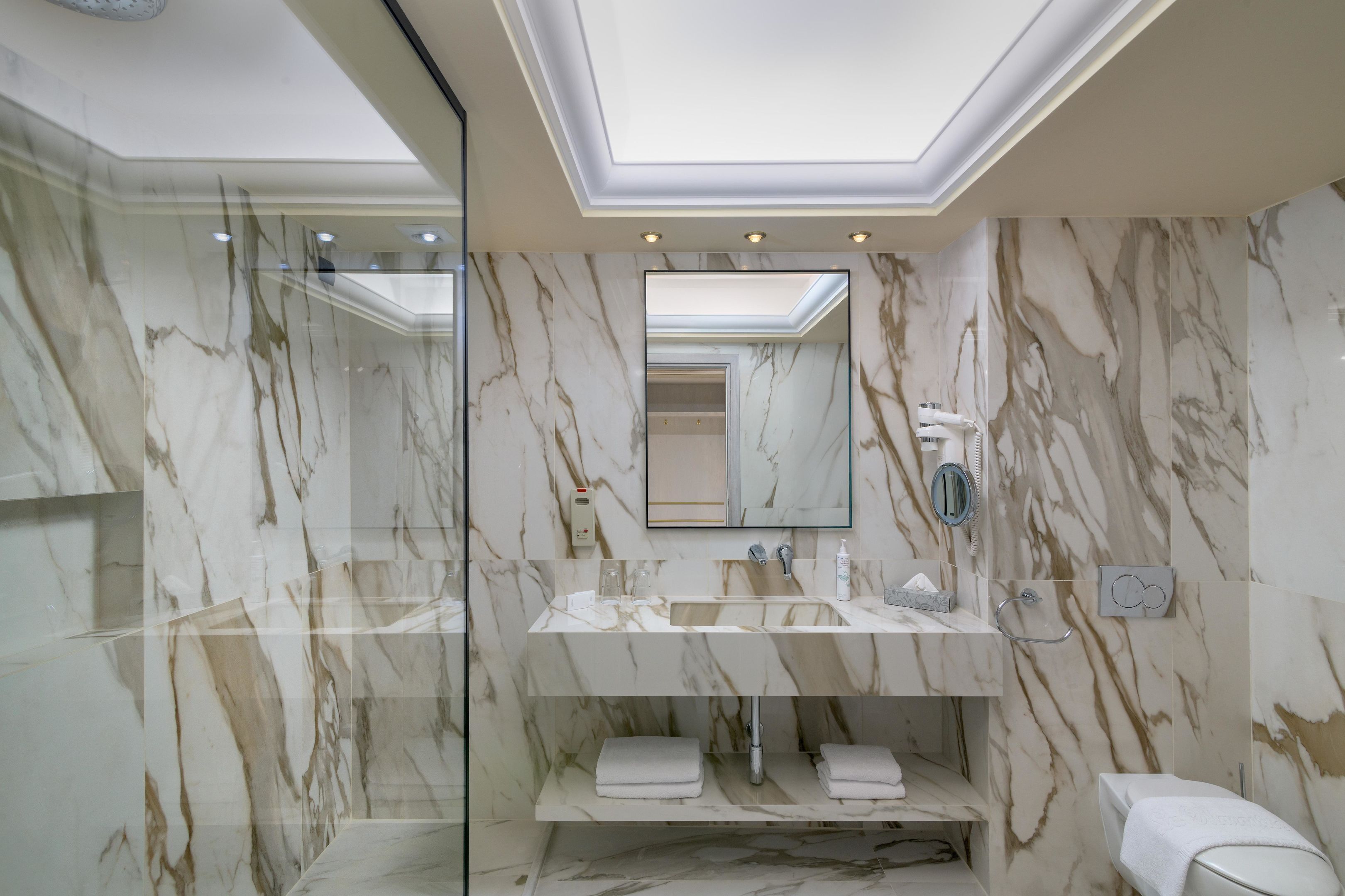 A modern bathroom with a glass-enclosed shower, a marble vanity, and a toilet.