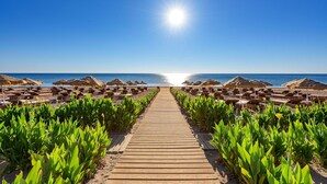 Ein hölzerner Weg führt zu Strandstühlen und Sonnenschirmen.