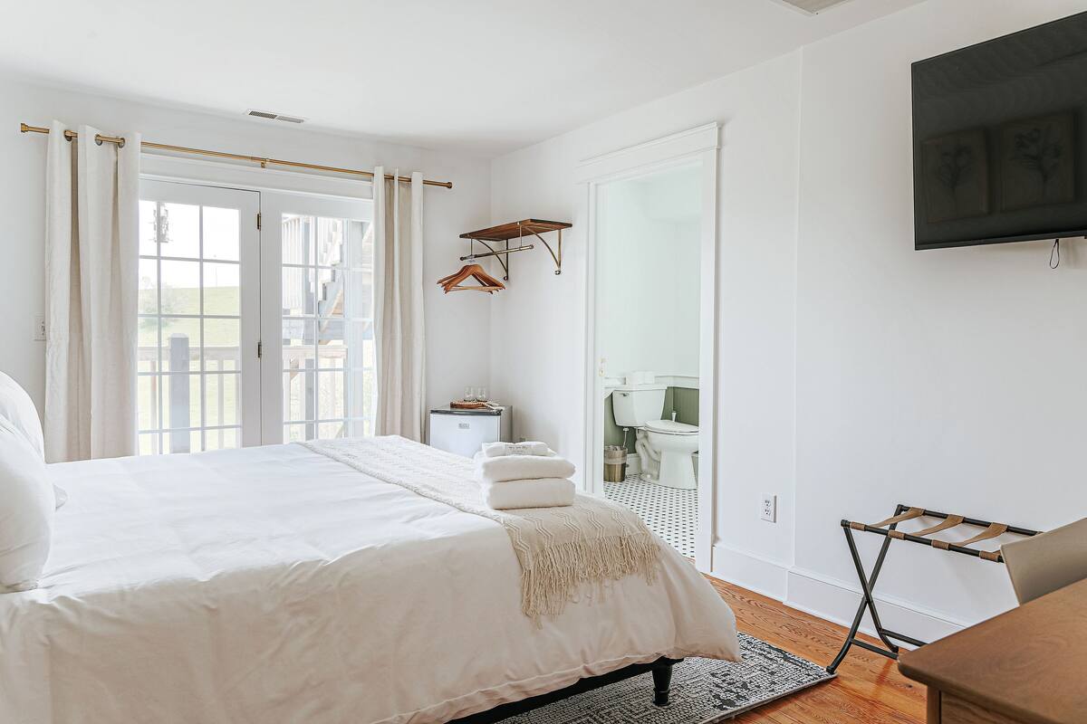 Quarto com uma cama grande, televisão fixada na parede e um varal de madeira.
