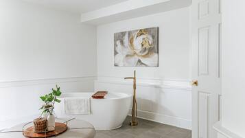 Un baño moderno con una bañera independiente, una puerta blanca y un cuadro abstracto grande en la pared.