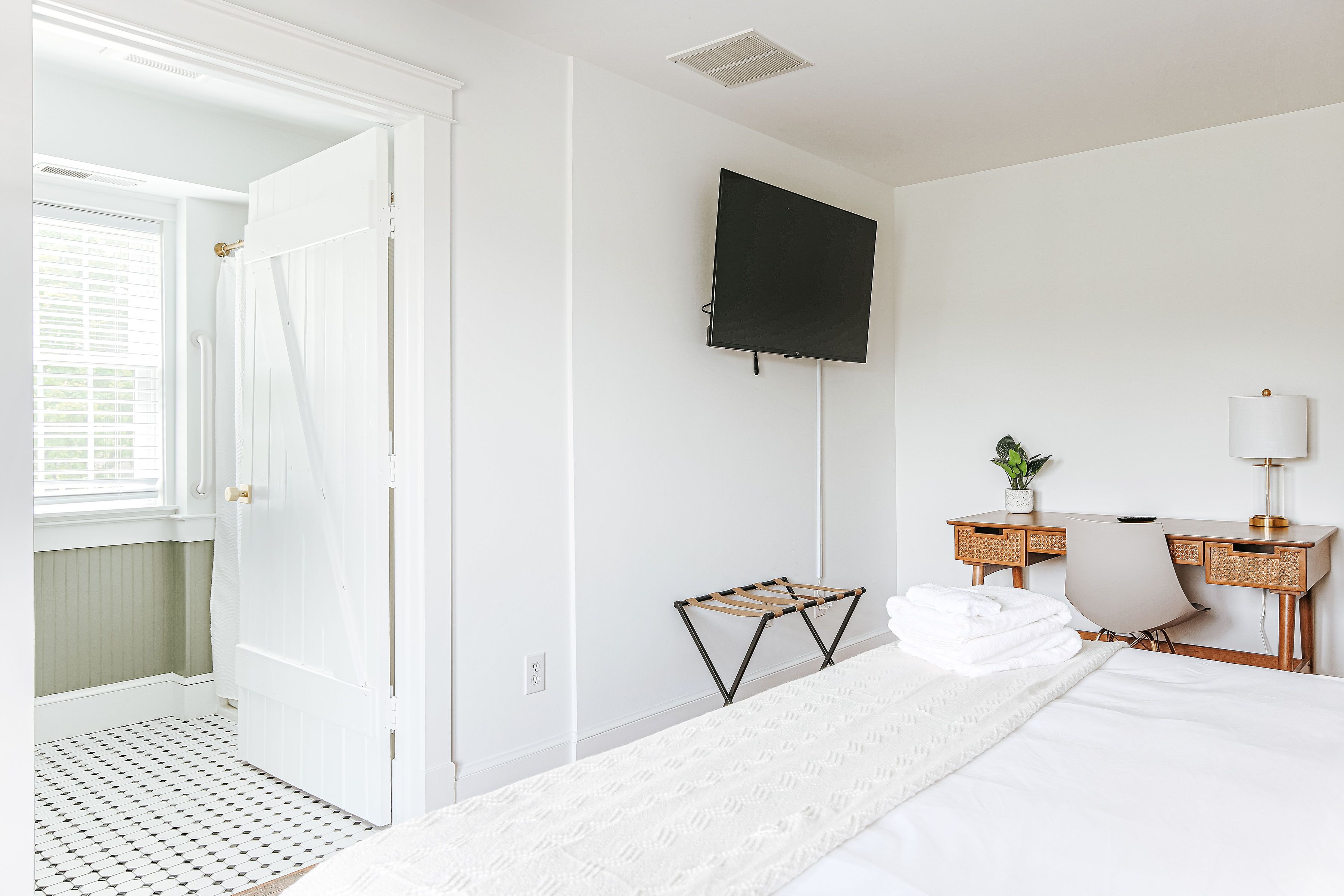 Quarto de hotel com uma cama, uma mesa com cadeira, uma televisão na parede e uma janela com persianas.