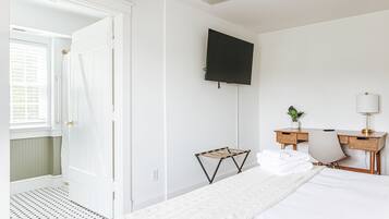 Quarto de hotel com uma cama, uma mesa com cadeira, uma televisão na parede e uma janela com persianas.