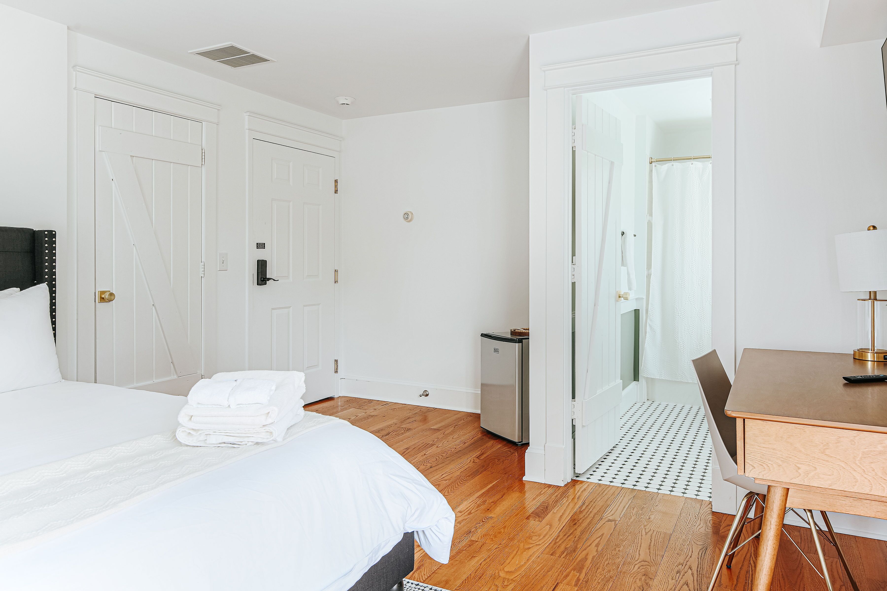 A hotel room with a bed, a desk, and a small refrigerator.