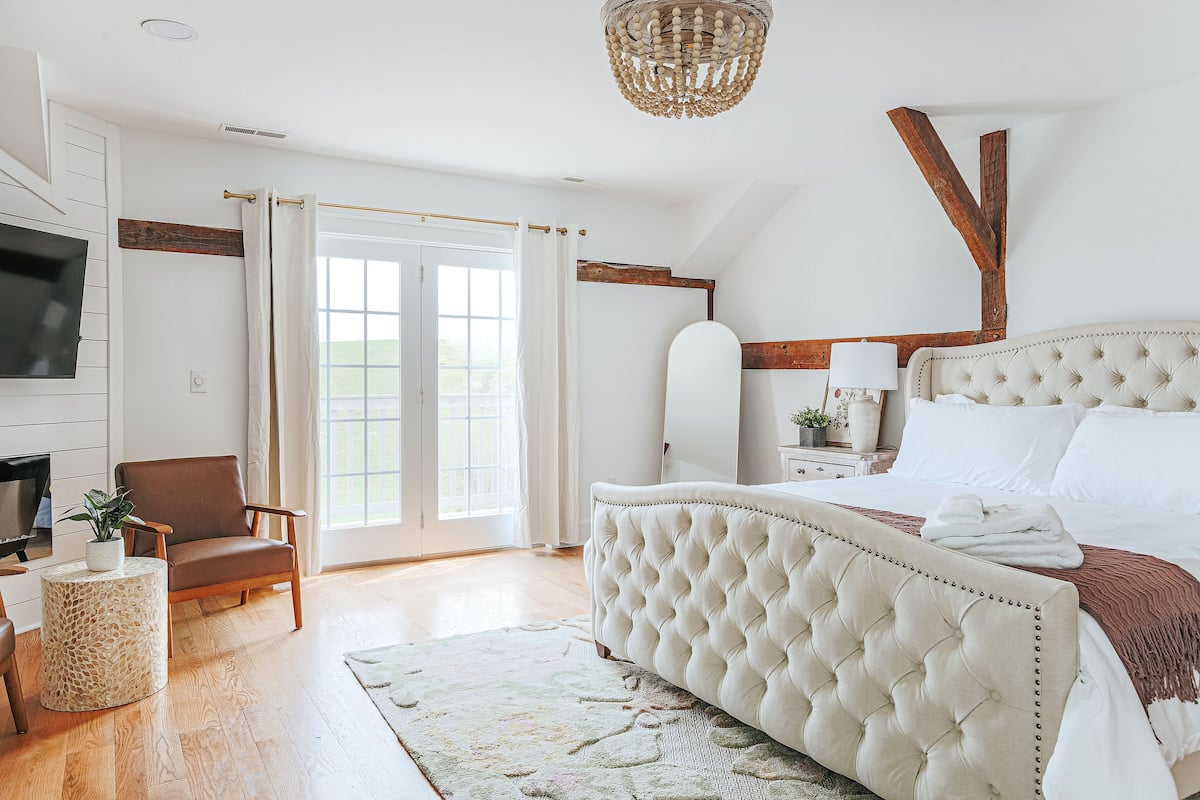 Quarto com uma cama grande, televisão, uma cadeira e janela com cortinas.