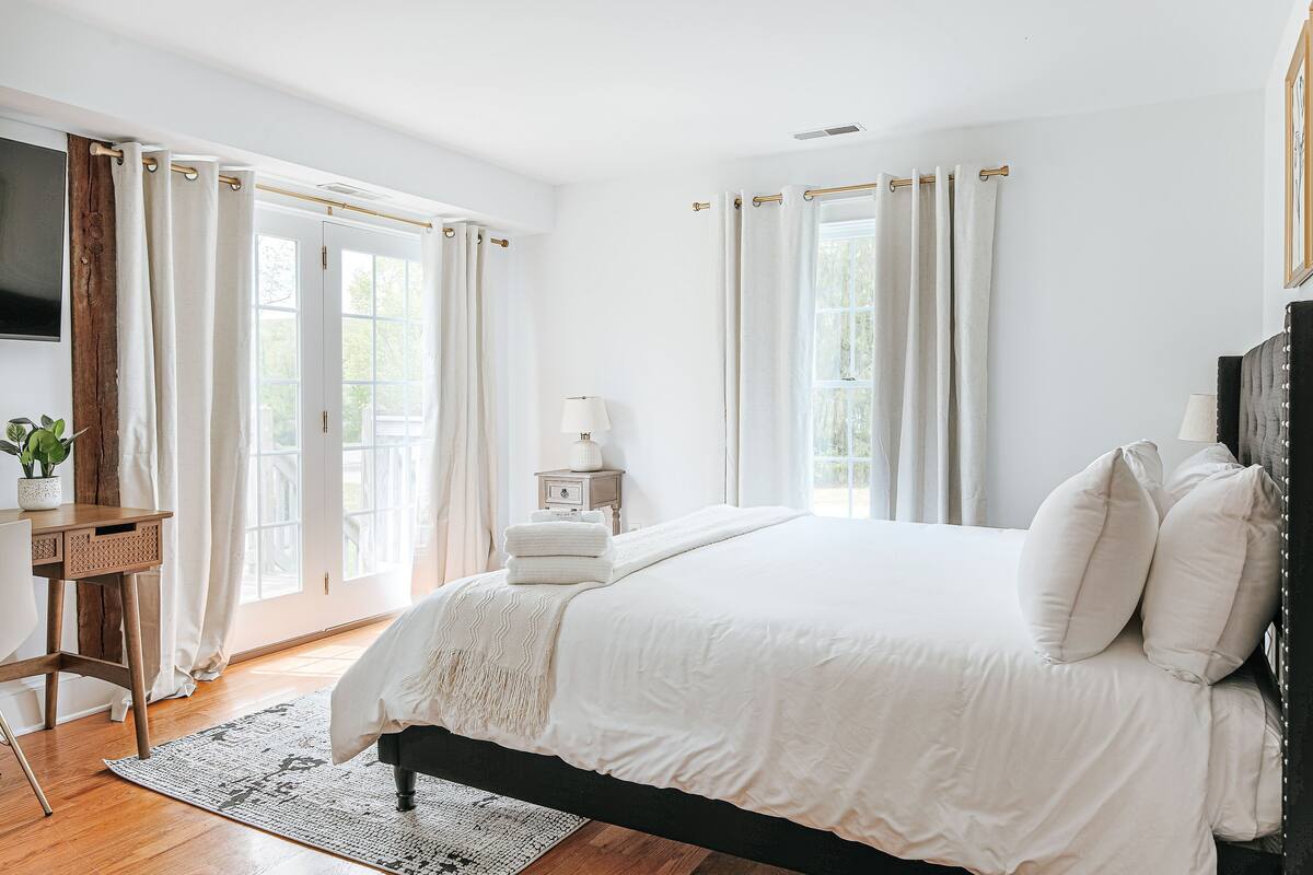 Quarto com uma cama grande, uma mesa de cabeceira com abajur e vista para o exterior pela janela.