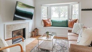 Una sala de estar con chimenea, un sofá, una mesa de centro de vidrio y un televisor montado en la pared.