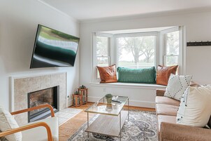 Una sala de estar con chimenea, un sofá, una mesa de centro de vidrio y un televisor montado en la pared.