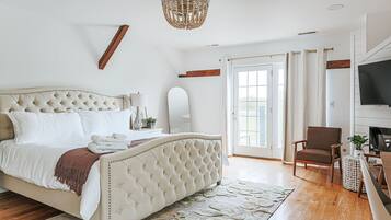 A bedroom with a large bed, a television, a chair, and a door leading to a balcony.