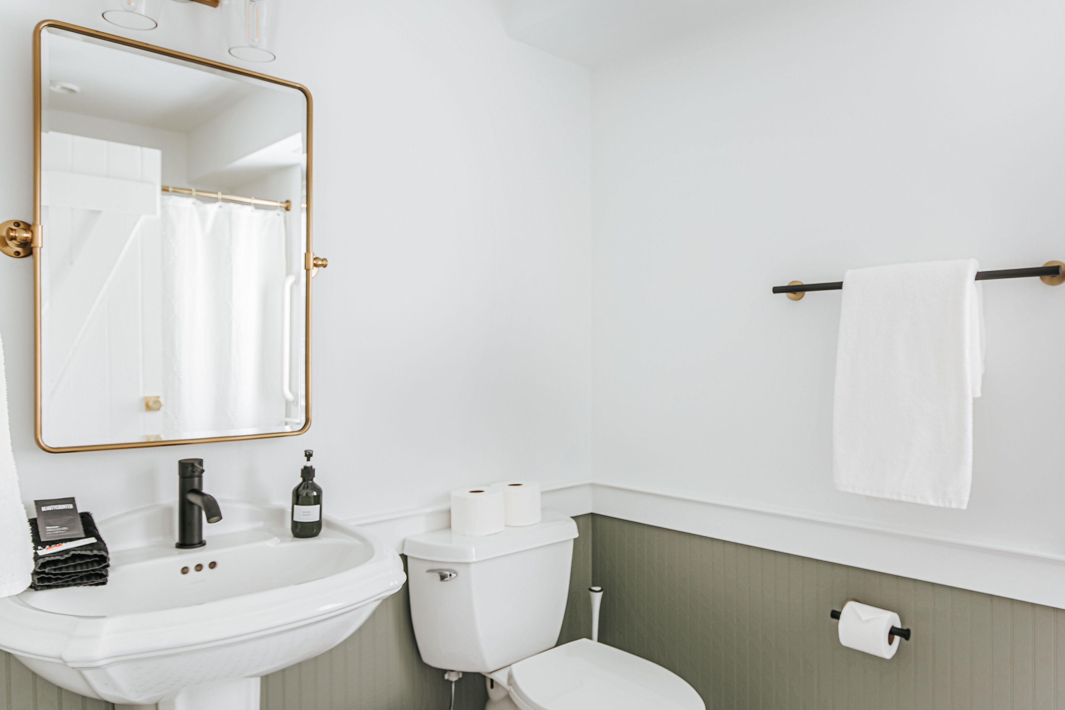 Une salle de bain avec un lavabo blanc, des toilettes, un miroir avec un cadre doré et un porte-serviettes sur lequel est posée une serviette blanche.