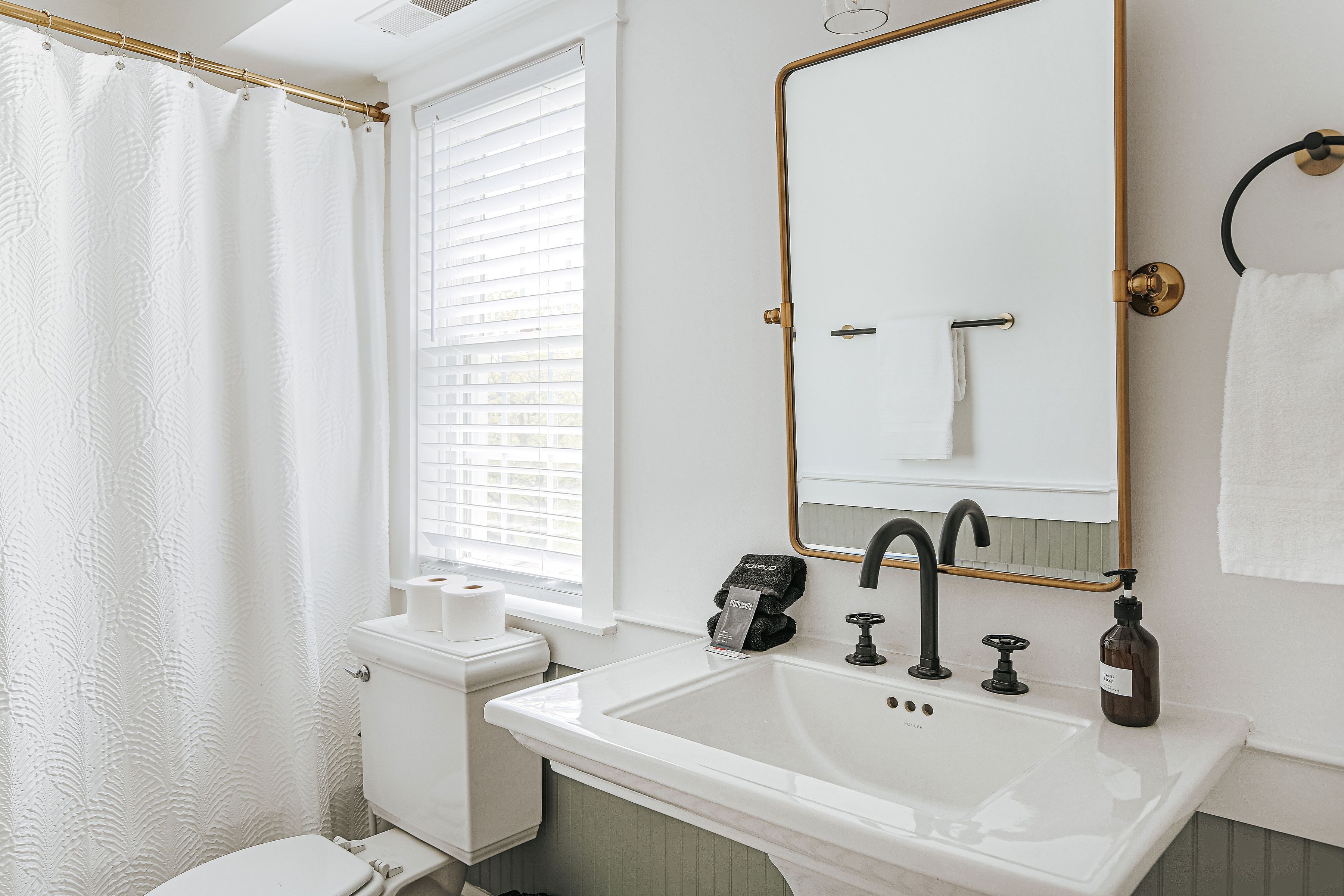 A bathroom with a white sink, black faucet, and a mirror with a gold frame.