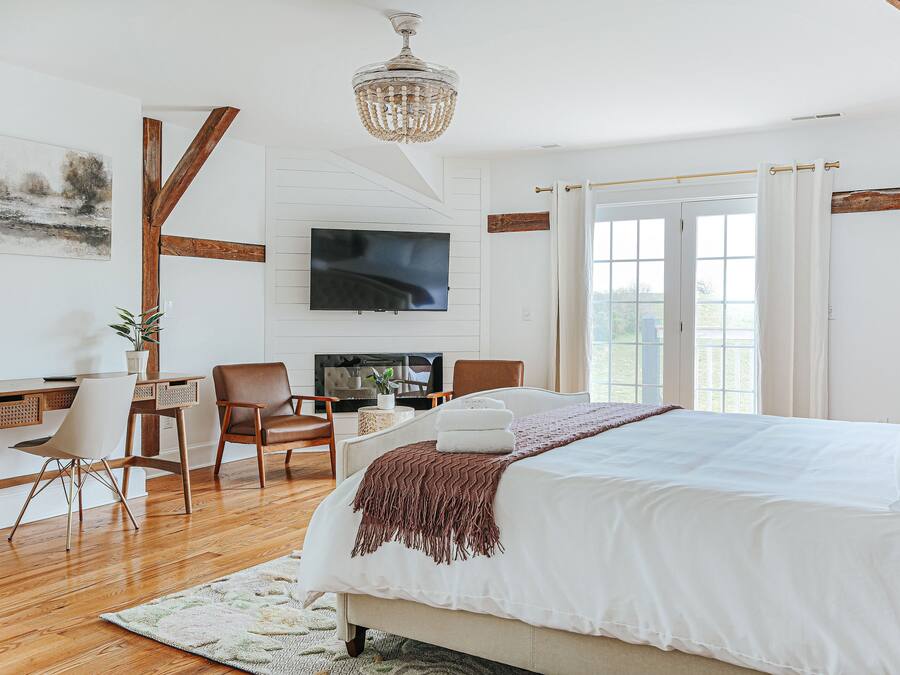 A bedroom with a large bed, a desk with a chair, a television, and a window with curtains.