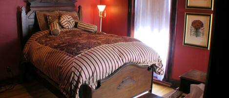 Une chambre avec un grand lit, une table de chevet, une lampe et une fenêtre avec des rideaux.