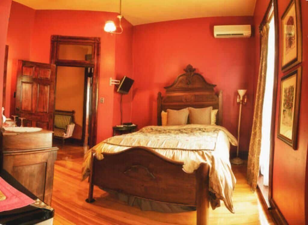 A bedroom with a wooden bed, a nightstand, a dresser, and a red wall.