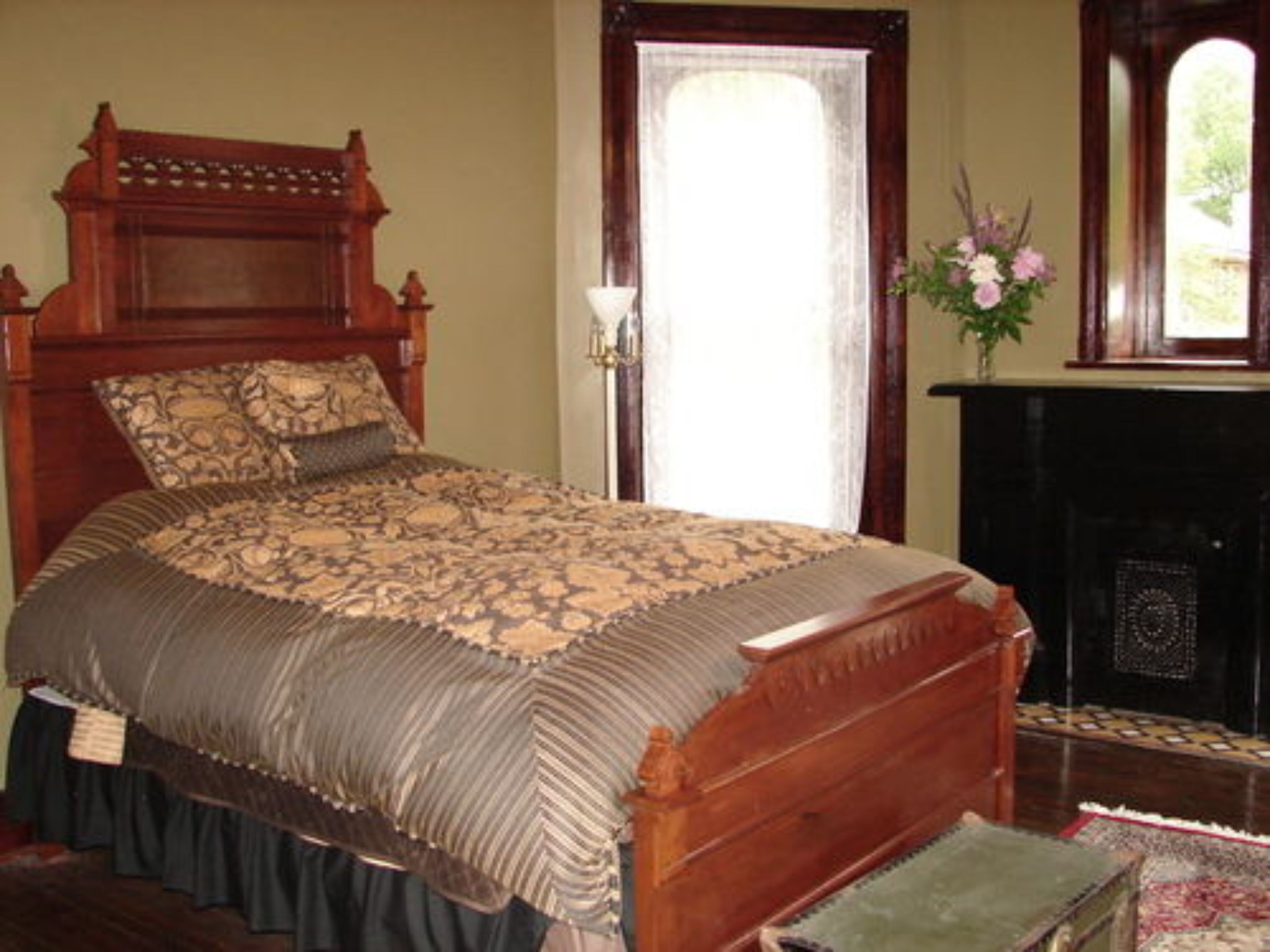 A traditional wooden bed with a patterned bedspread, a fireplace, and a window with curtains.