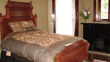 A traditional wooden bed with a patterned bedspread, a fireplace, and a window with curtains.