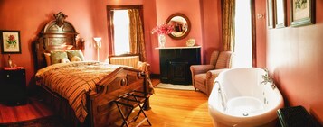 A bedroom with a wooden bed, a large mirror, a fireplace, a sitting area, and a bathtub.