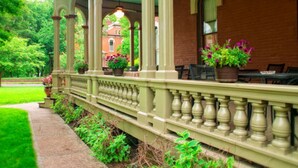 Un porche cubierto con columnas, plantas en macetas y un muro de ladrillo.
