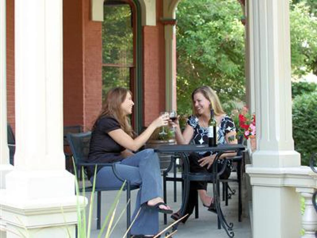 Two people sitting at an outdoor table with a brick wall and greenery in the background.