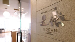 A modern interior with a glass partition and a wall-mounted sign reading "GOKAN OKAMURA MODERN WINING."