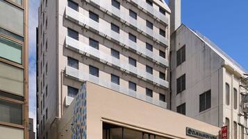 Ein mehrstöckiges Hotel mit moderner Fassade, einer überdachten Eingangsparte und einem Parkplatz mit Verkaufsautomaten.