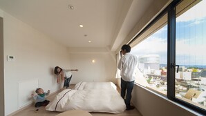 A modern hotel room with a large window, a bed, a small table, and a child playing.