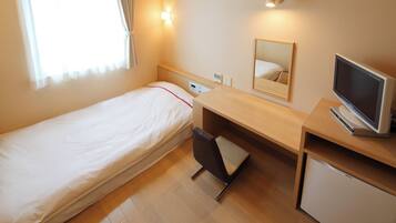 A hotel room with a single bed, a desk with a computer, a small refrigerator, and a mirror.