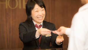 A person in a black suit and red polka dot tie at a reception desk with a name tag.