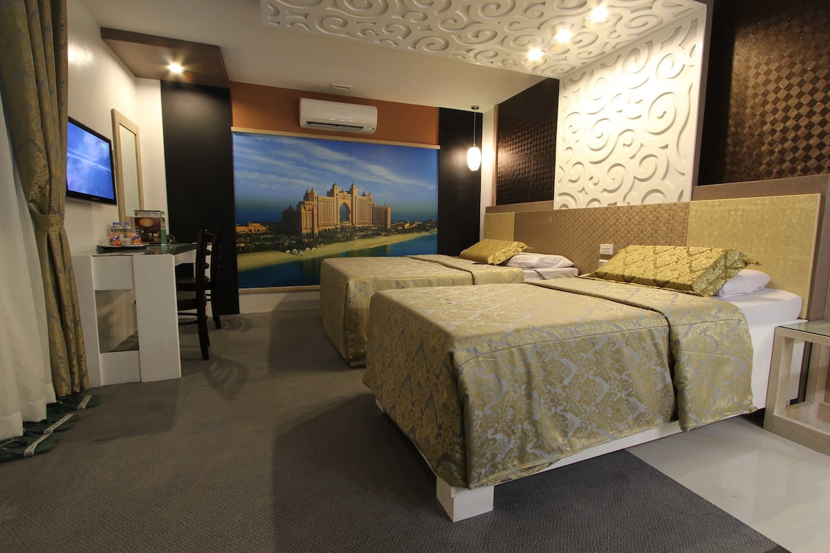 A hotel room with two beds, a desk with a computer, a flat-screen TV, and a large mural of a castle.