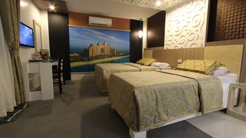 Habitación de hotel con dos camas, un escritorio con computadora, televisor de pantalla plana y un gran mural de un castillo.