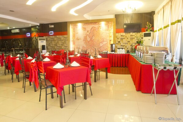 A banquet hall with tables set for a formal event, featuring a large map on the back wall and a buffet area with stacked plates.