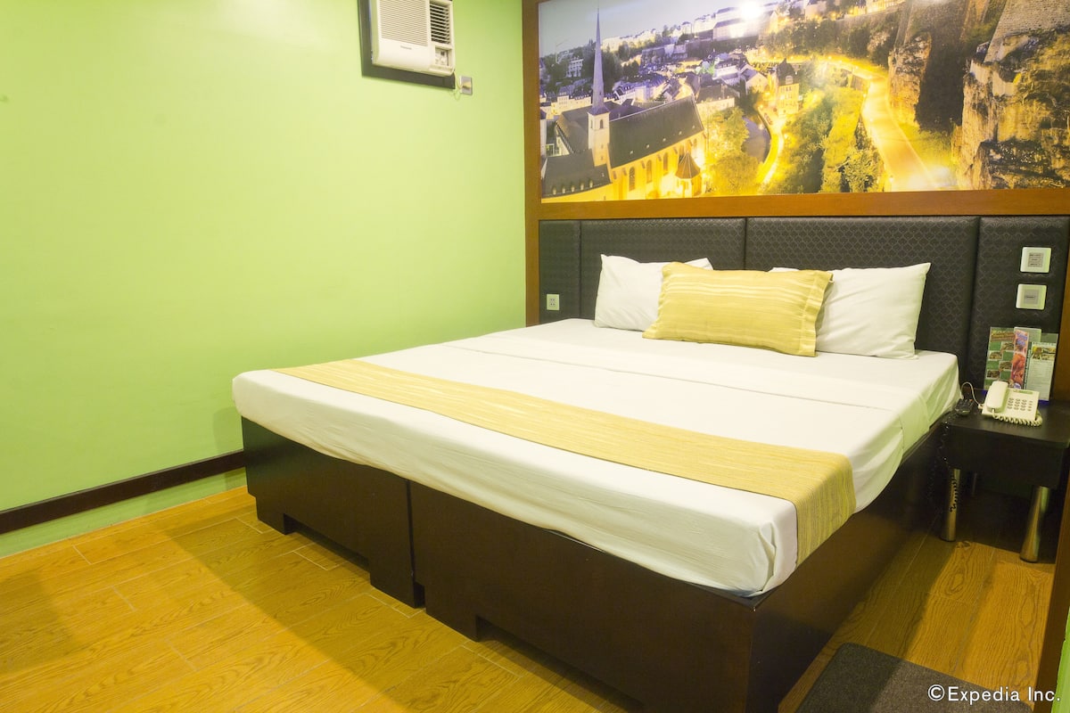 A hotel room with a bed, a nightstand, and a wall-mounted air conditioner.