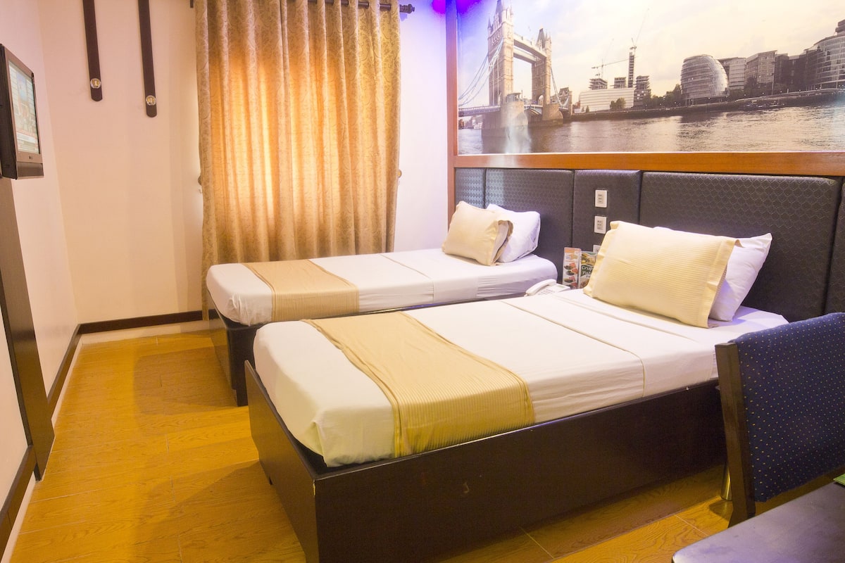 A hotel room with two beds, a view of a cityscape, and a wooden floor.