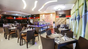 A restaurant with multiple dining tables and chairs, a bar area, and a wall-mounted television. - Eurotel Makati (Makati)