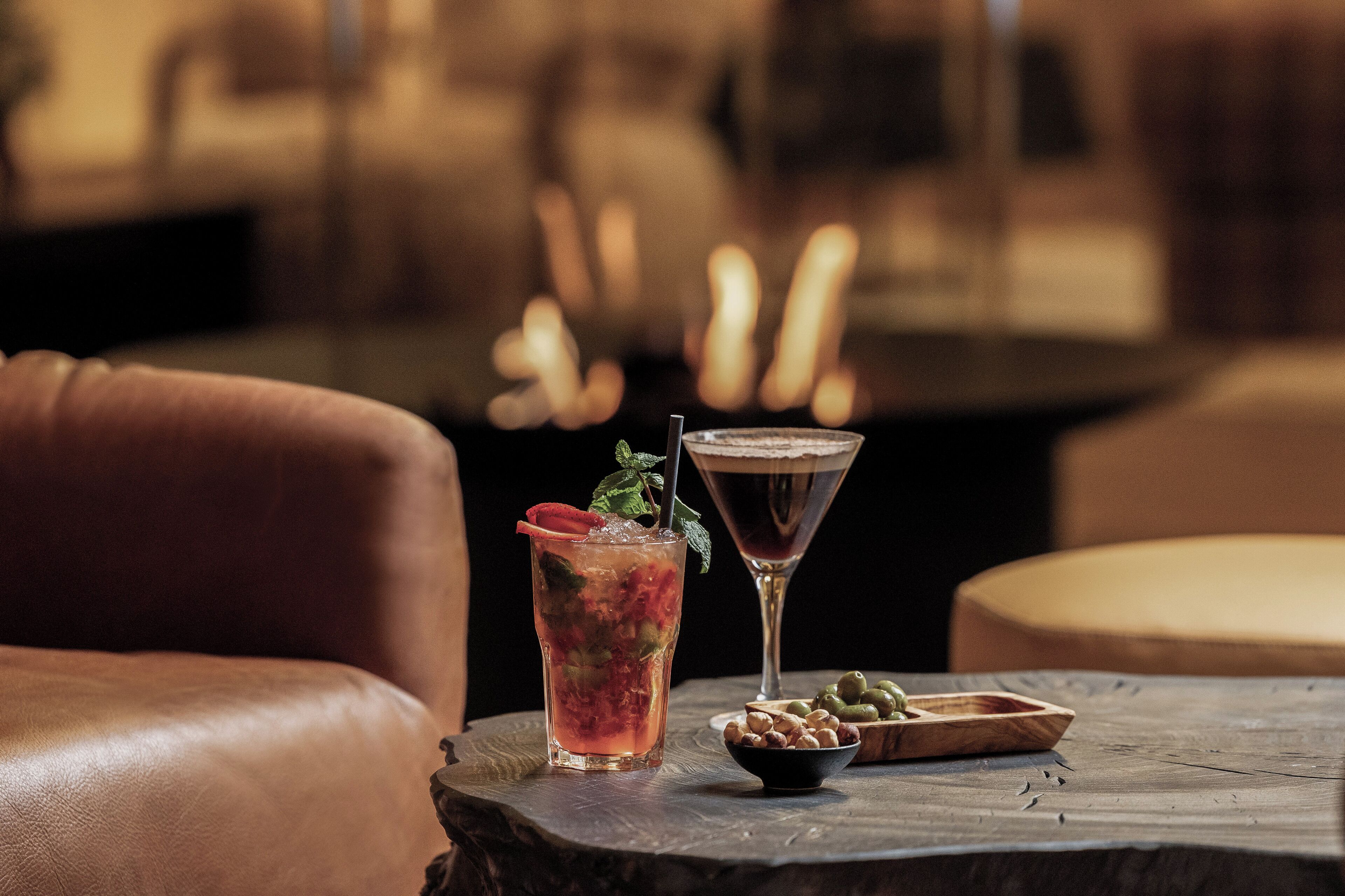 Un cóctel sobre una mesa de madera, con una copa de martini y una bebida adornada con una fresa.