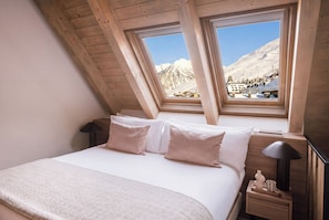 A bedroom with a bed, pillows, a bedside table with a lamp, and a view of a snowy mountain landscape through a window. - MIM Baqueira Member of Meliá Collection (Naut Aran)
