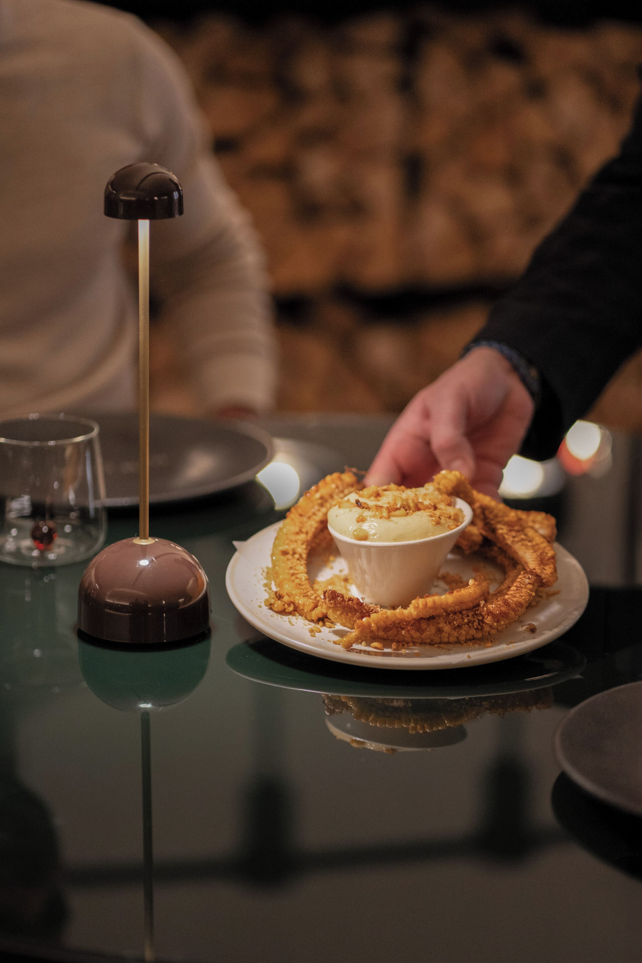 A dessert with a chocolate dome on a plate, accompanied by a glass of wine and a fork.