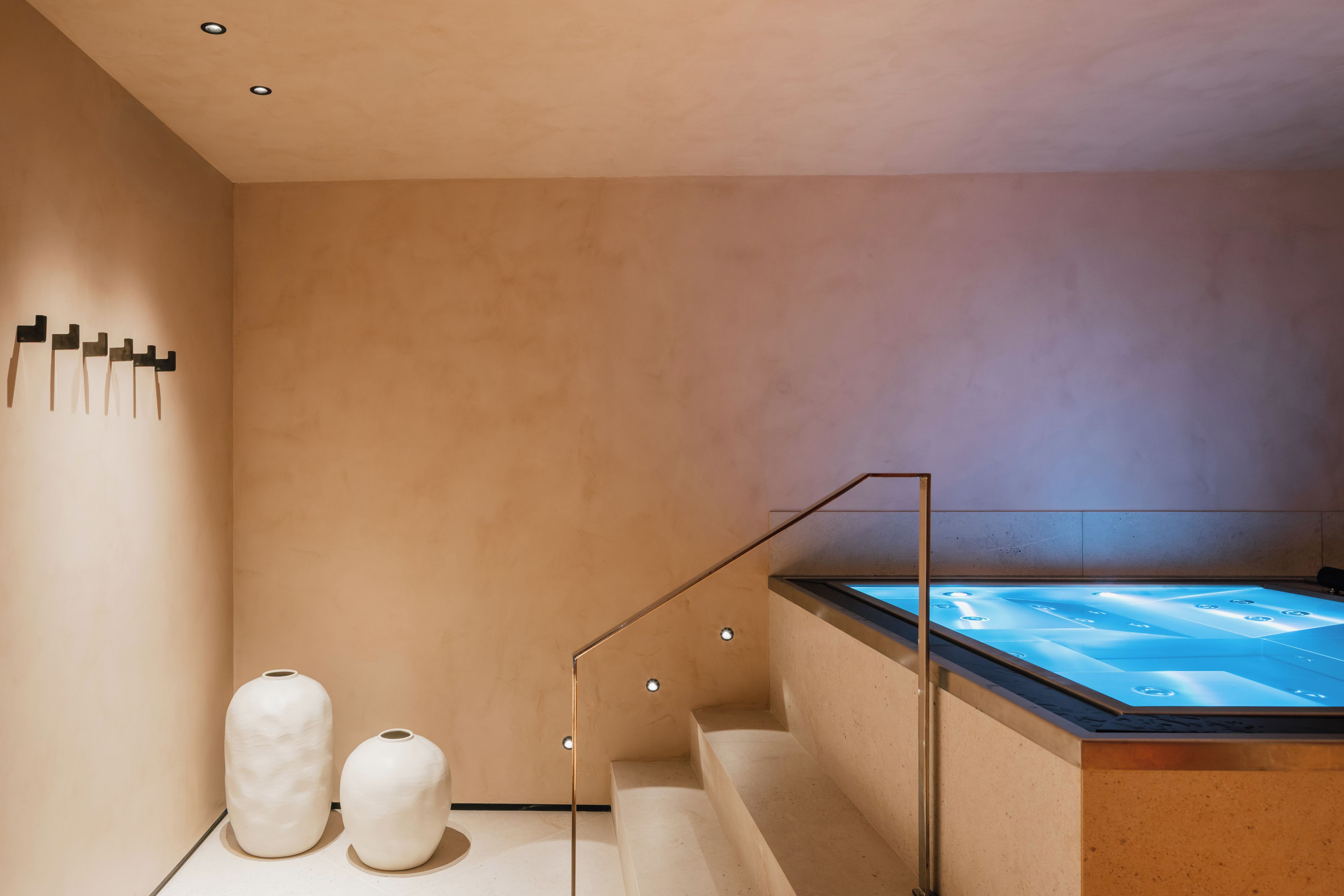 A modern spa room with a heated floor, a large bathtub, and two white vases on the floor.