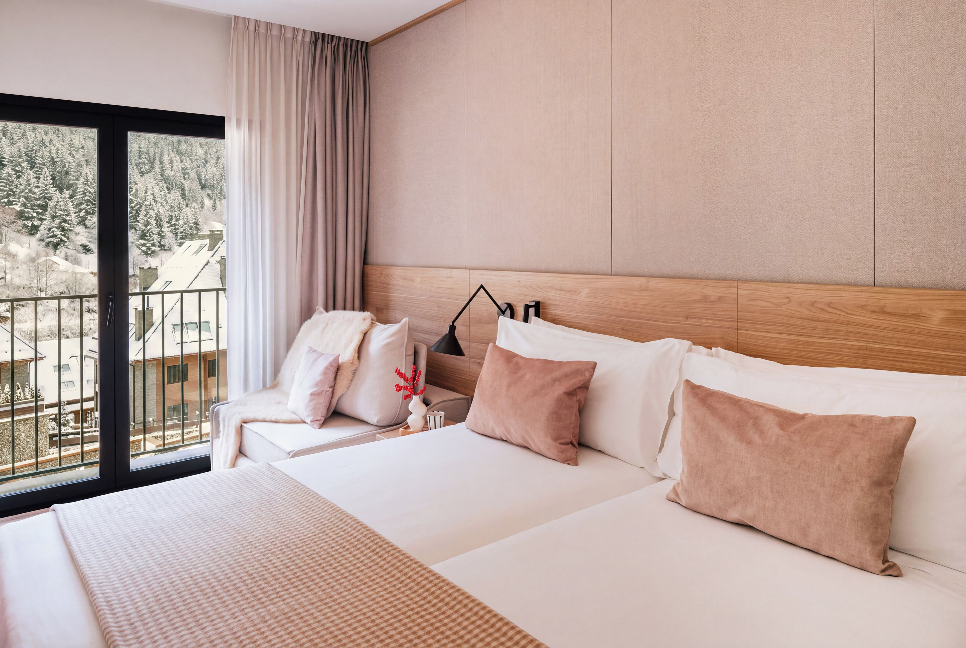 A hotel room with a large bed, a nightstand, a lamp, and a view of a snowy landscape through the window.