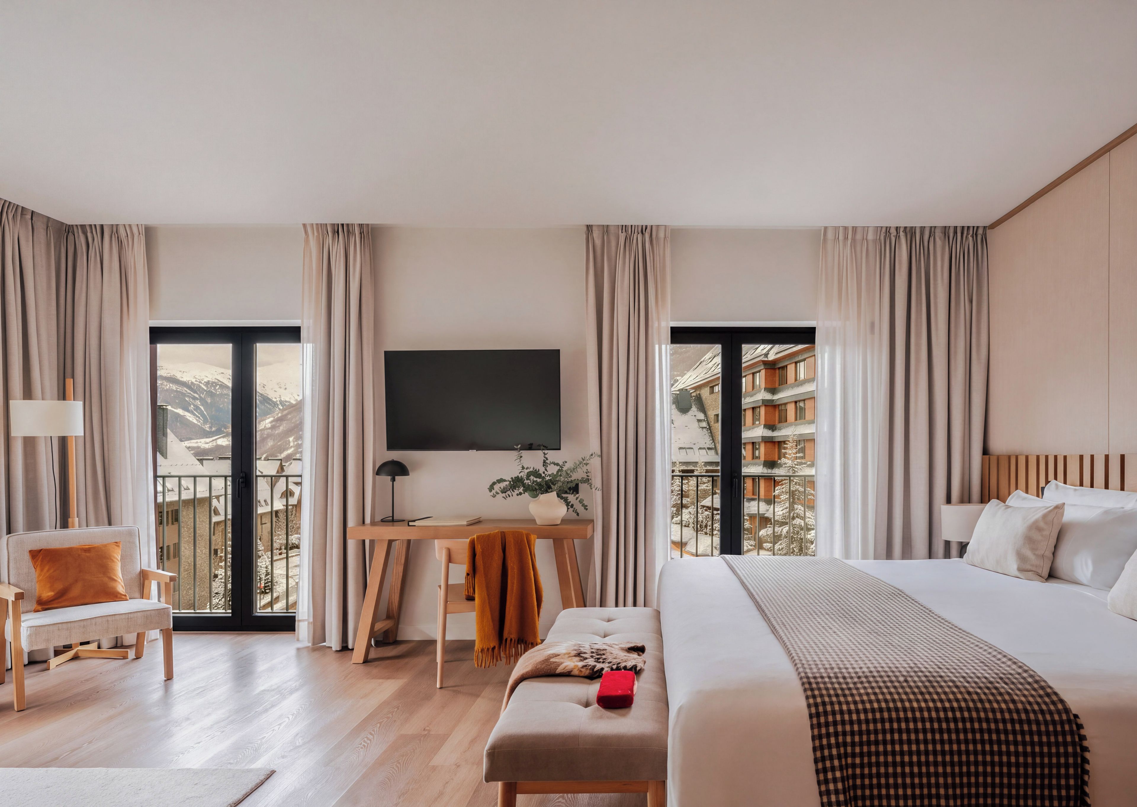 Habitación de hotel con cama, escritorio con silla, televisión y vistas a edificios nevados.