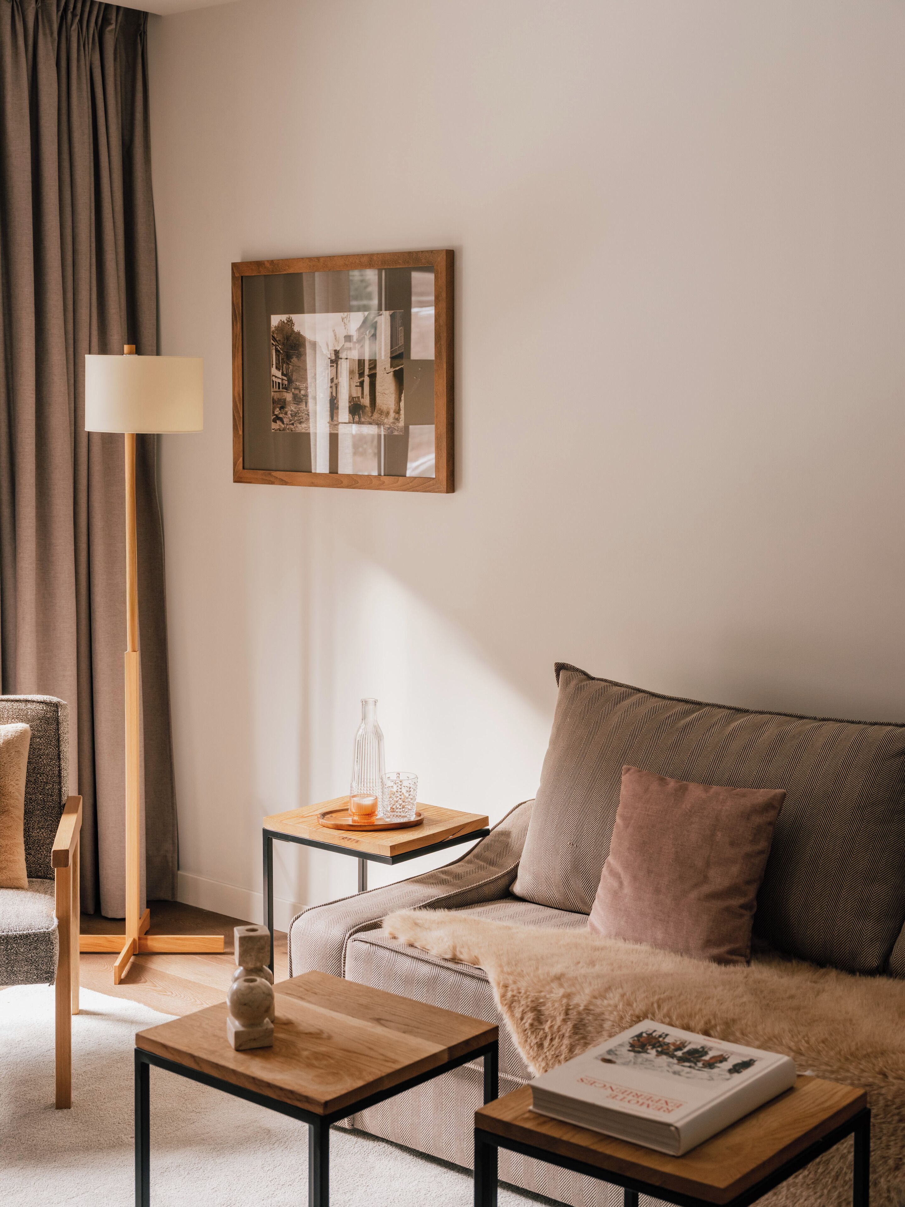 Una sala de estar acogedora con un sofá, una mesita de centro, una lámpara de pie, una mesita auxiliar con una vela y un cuadro en la pared.