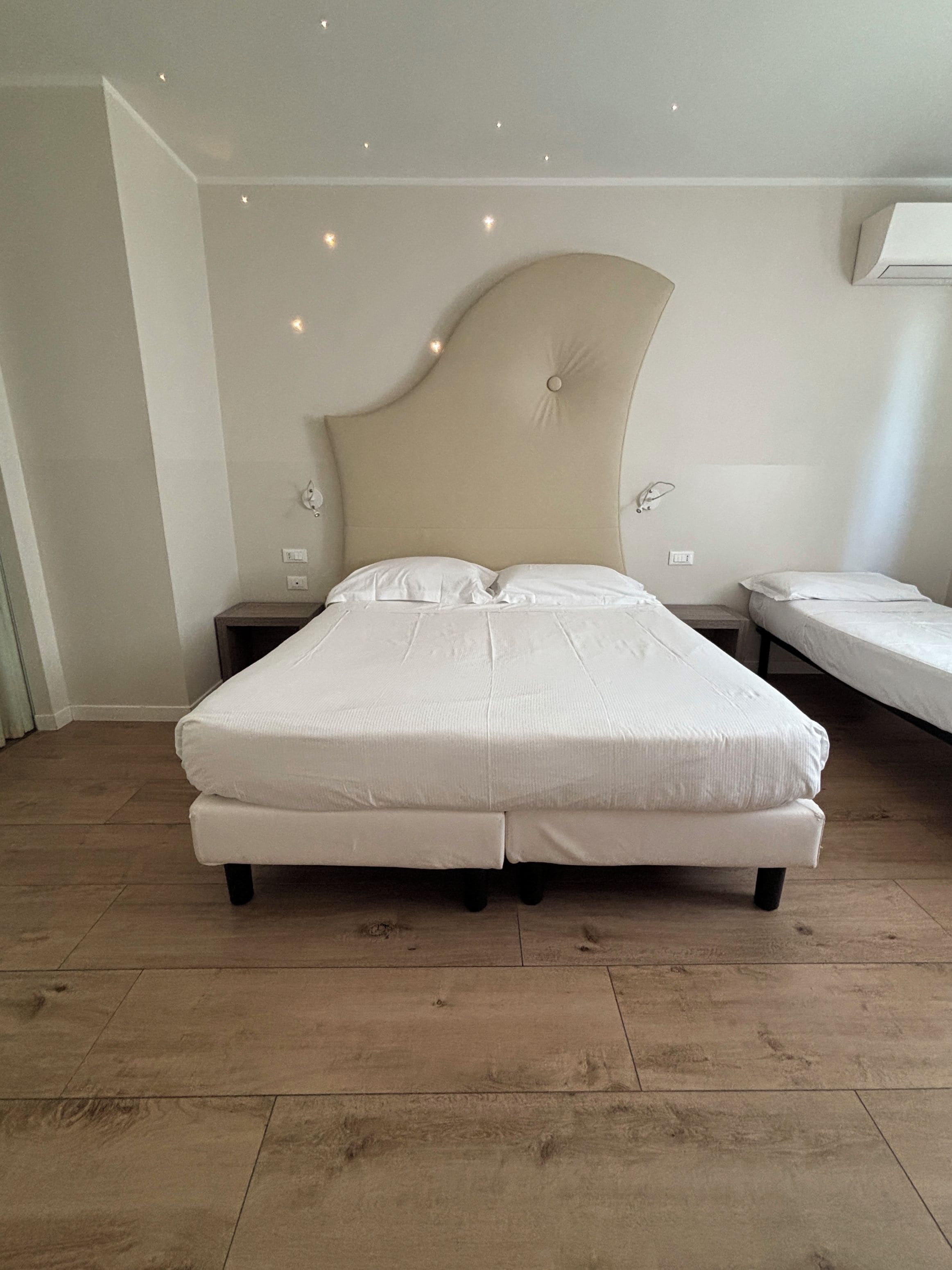 A bedroom with a large bed, two bedside tables, and a wall-mounted air conditioning unit.