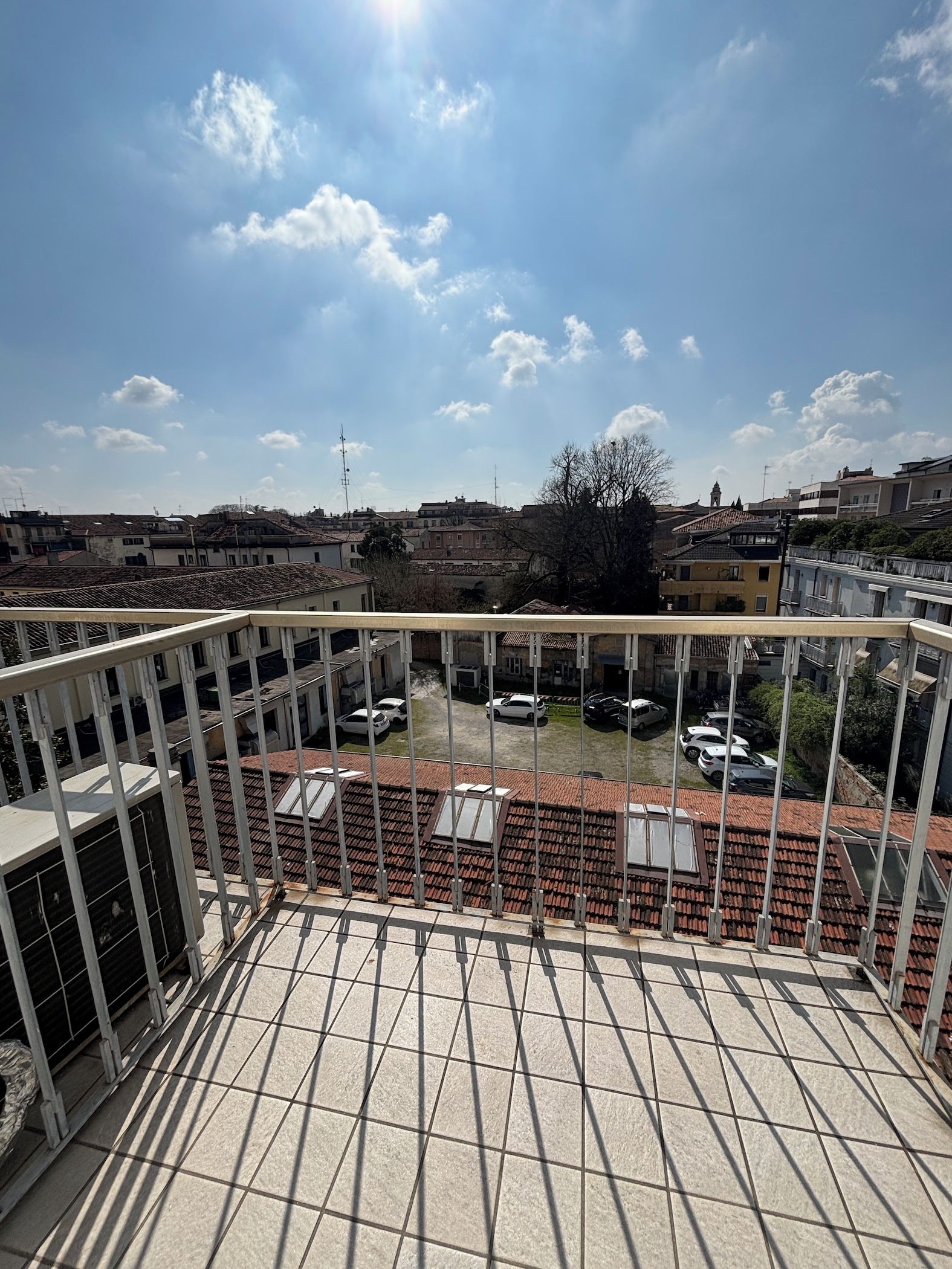 Terraza en la azotea con vistas a un barrio residencial, con barandilla metálica y cielo despejado.